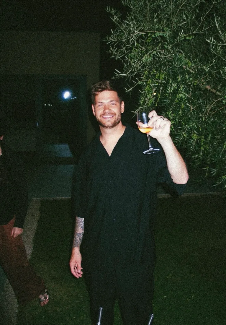 Julian in a garden at night with a glass of wine